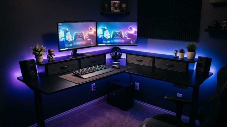 FlexiSpot L-shaped standing desk with rear shelf, two monitors and four fabric drawers in a purple-lit gaming corner
