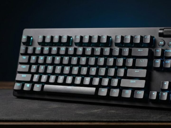 Black tenkeyless gaming keyboard with aluminium front plate, blue backlight, media buttons and volume roller on a dark desk